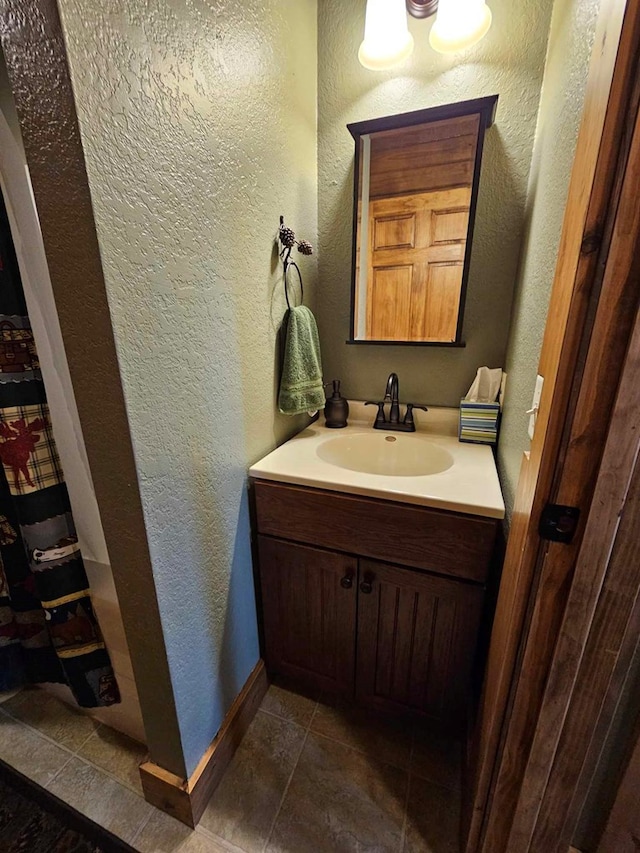 bathroom with a textured wall, baseboards, and vanity
