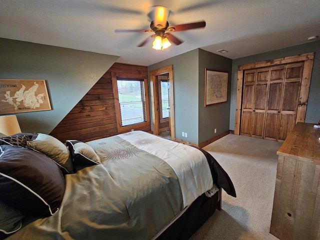 bedroom with light carpet, baseboards, a ceiling fan, wood walls, and a closet