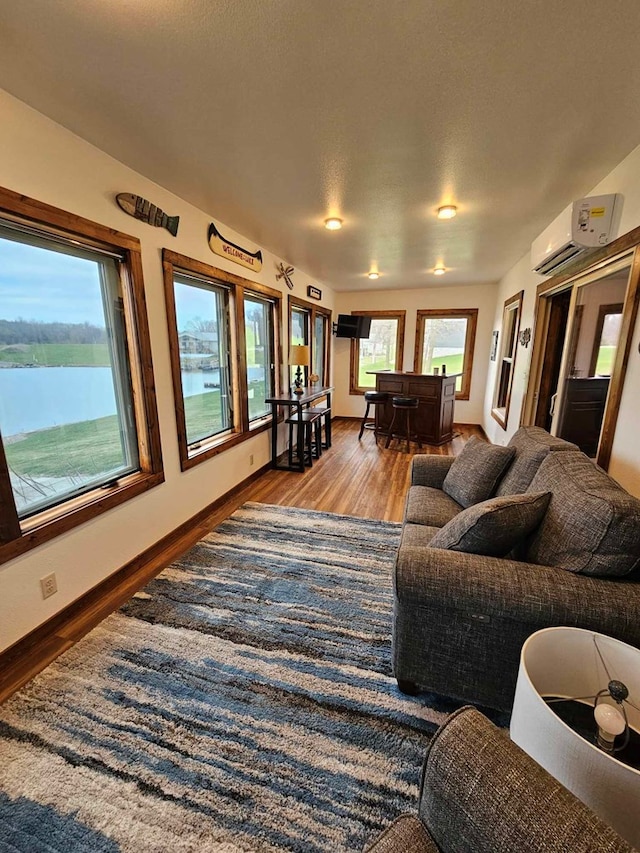 living area with baseboards, wood finished floors, and a wall unit AC