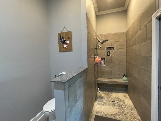 bathroom featuring a tile shower, crown molding, and toilet