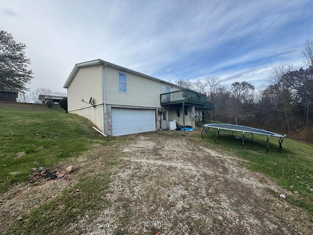 view of side of property with a lawn, a garage, a trampoline, and a wooden deck