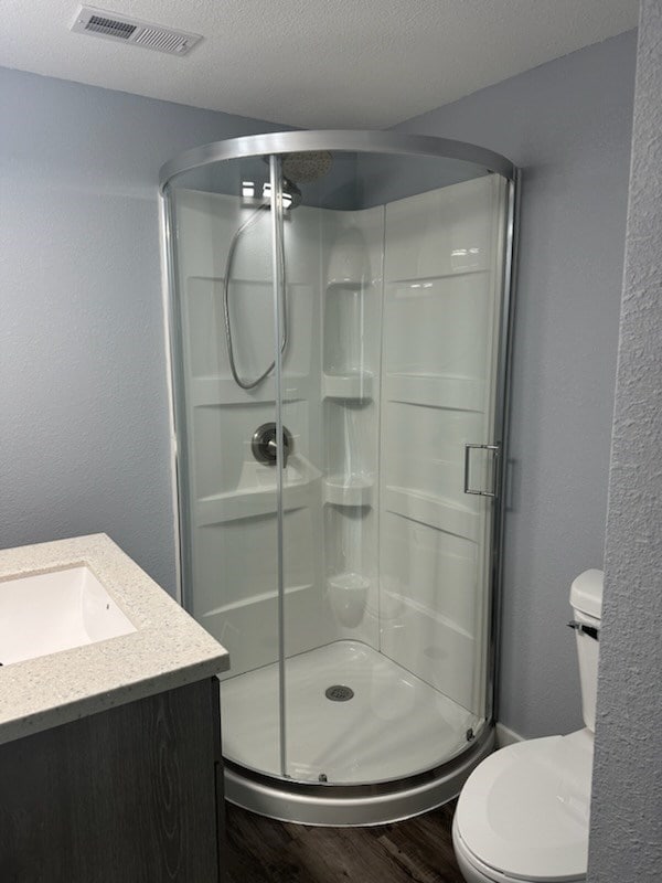 bathroom with hardwood / wood-style floors, vanity, toilet, a textured ceiling, and an enclosed shower