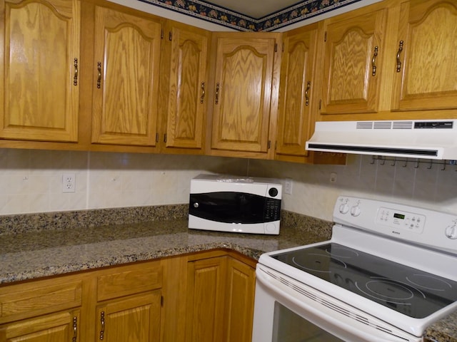 kitchen featuring white appliances, backsplash, light stone counters, and range hood