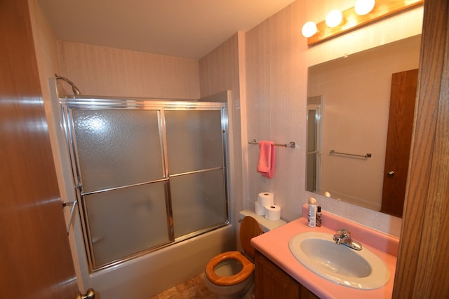 bathroom with wallpapered walls, toilet, vanity, and bath / shower combo with glass door