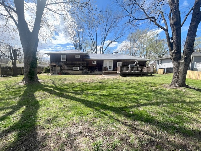 rear view of property with a wooden deck, metal roof, fence, and a lawn