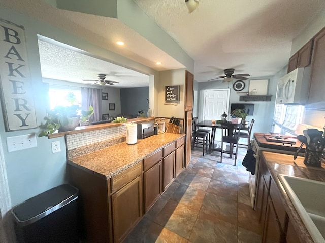 kitchen featuring a sink, a ceiling fan, a textured ceiling, white microwave, and gas stove