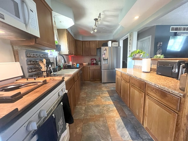 kitchen with stainless steel fridge with ice dispenser, range, white microwave, stone finish floor, and a sink