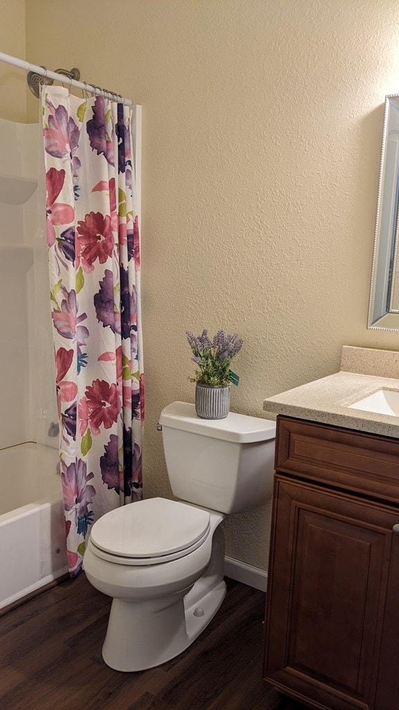 full bathroom with hardwood / wood-style floors, vanity, shower / bath combination with curtain, and toilet