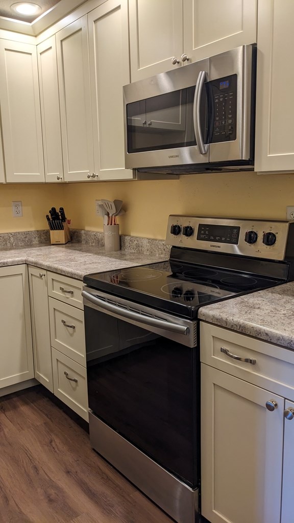 kitchen with appliances with stainless steel finishes, dark hardwood / wood-style floors, and white cabinetry