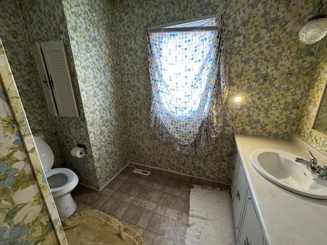 bathroom with toilet, vanity, visible vents, and wallpapered walls