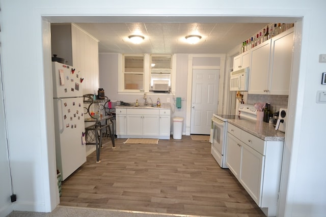 kitchen featuring decorative backsplash, a sink, white cabinets, light wood finished floors, and white appliances