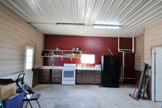 kitchen featuring white electric range oven, a sink, wood walls, concrete floors, and freestanding refrigerator