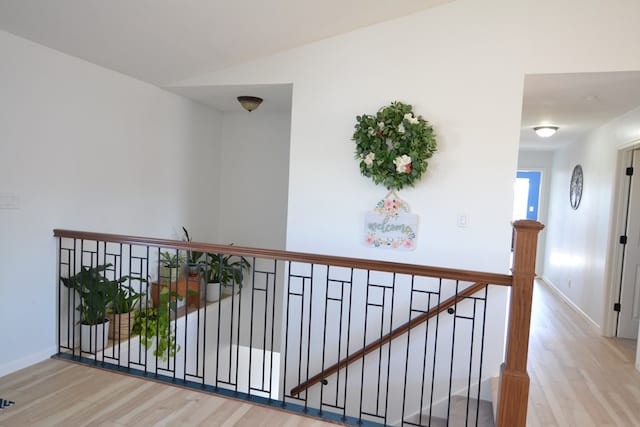 hall with baseboards, wood finished floors, and an upstairs landing
