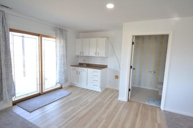 kitchen featuring white cabinets, dark countertops, a sink, light wood-style floors, and backsplash