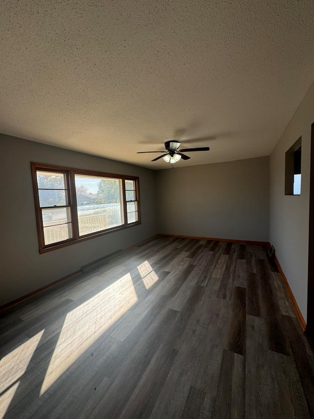 empty room with dark wood-style flooring, ceiling fan, a textured ceiling, and baseboards