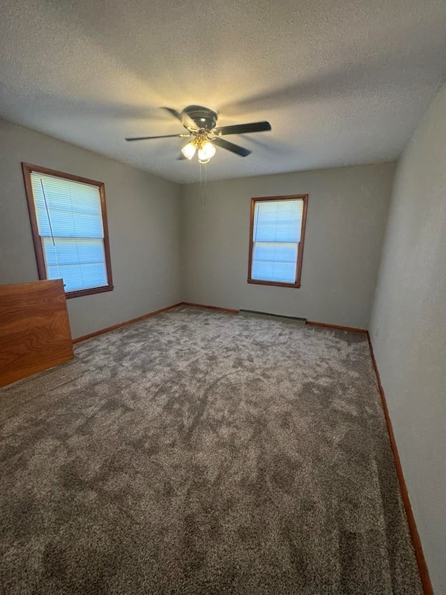 carpeted spare room with a ceiling fan, a textured ceiling, baseboards, and a wealth of natural light