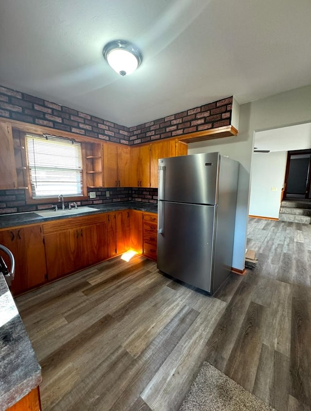 kitchen with brown cabinetry, dark wood-style floors, brick wall, freestanding refrigerator, and a sink