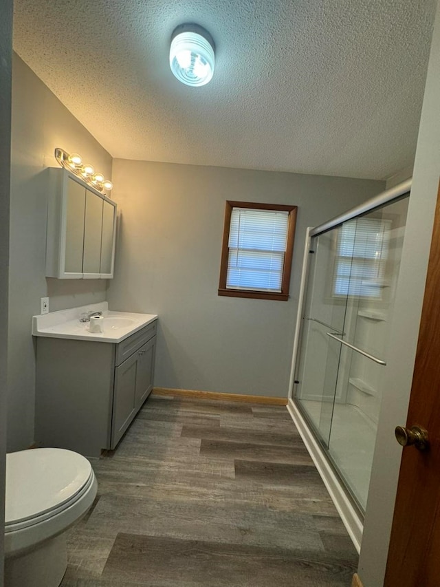 bathroom featuring toilet, wood finished floors, a textured ceiling, vanity, and a shower stall