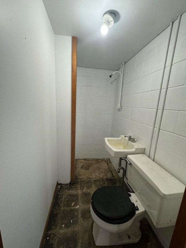 bathroom with toilet, a sink, and concrete block wall