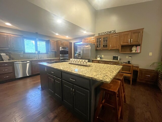kitchen featuring glass insert cabinets, stainless steel appliances, dark wood finished floors, a kitchen island, and light stone counters