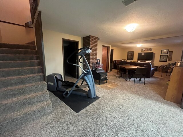 exercise area featuring a textured ceiling, a wood stove, visible vents, and carpet floors