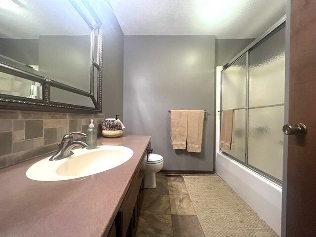 bathroom with toilet, vanity, decorative backsplash, and shower / bath combination with glass door