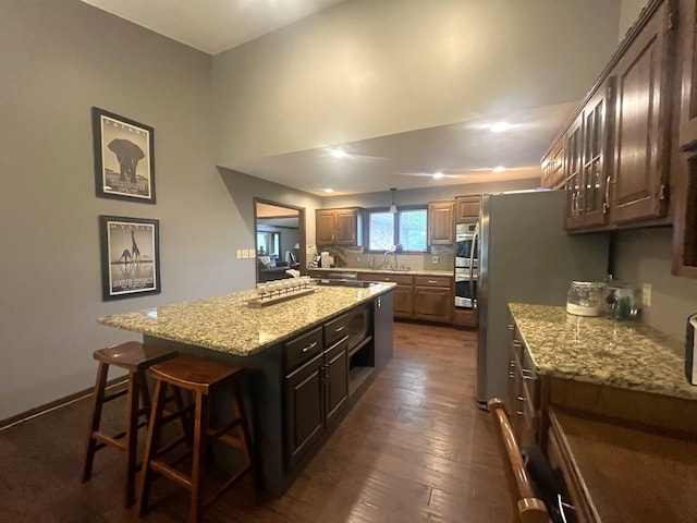 kitchen featuring a kitchen island, light stone countertops, double oven, a kitchen bar, and dark wood finished floors