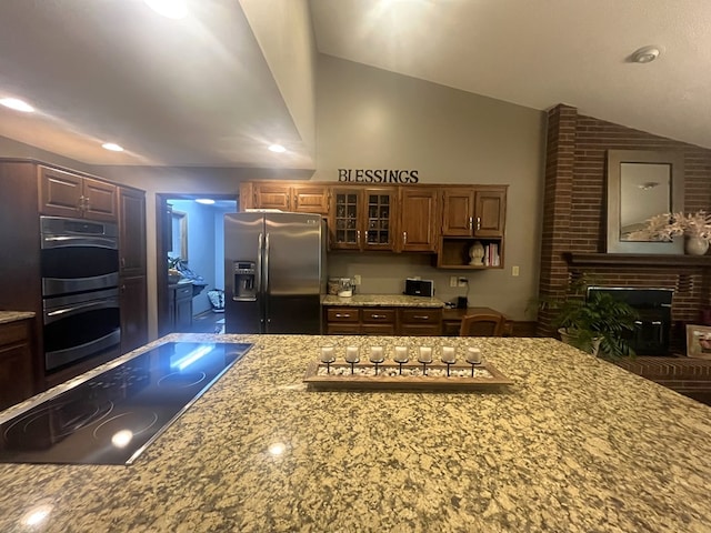 kitchen with appliances with stainless steel finishes, glass insert cabinets, vaulted ceiling, and light stone counters