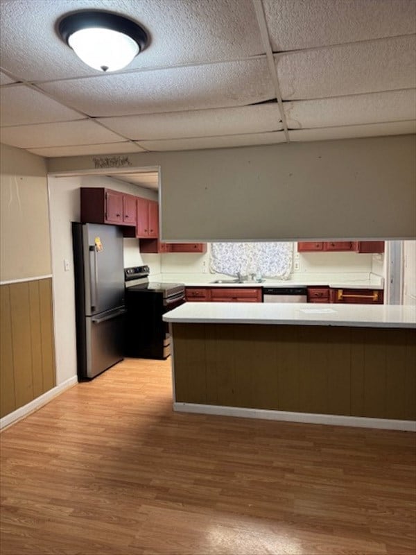 kitchen with sink, a drop ceiling, kitchen peninsula, light hardwood / wood-style floors, and appliances with stainless steel finishes