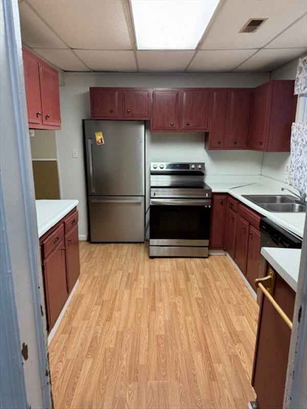 kitchen with a drop ceiling, sink, stainless steel appliances, and light hardwood / wood-style flooring