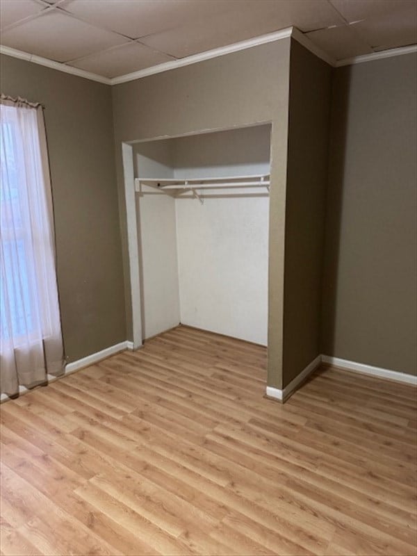 unfurnished bedroom with light wood-type flooring, multiple windows, and ornamental molding