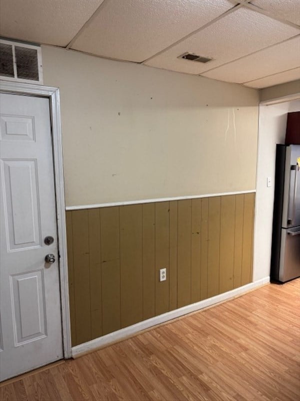 interior space with stainless steel fridge, wood walls, a drop ceiling, and light wood-type flooring