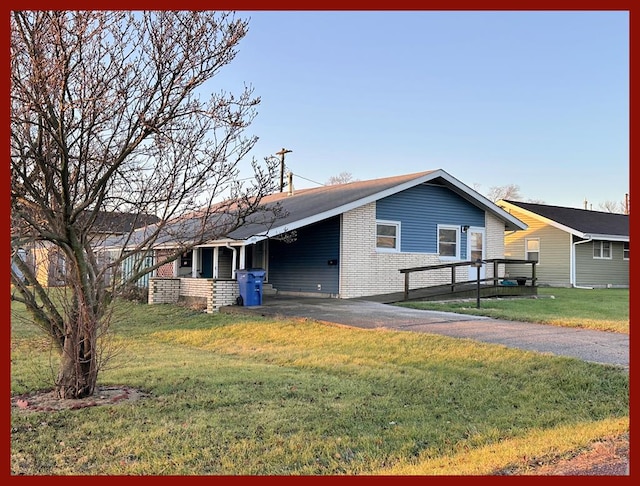 view of front of property featuring driveway, a front yard, an attached carport, and brick siding