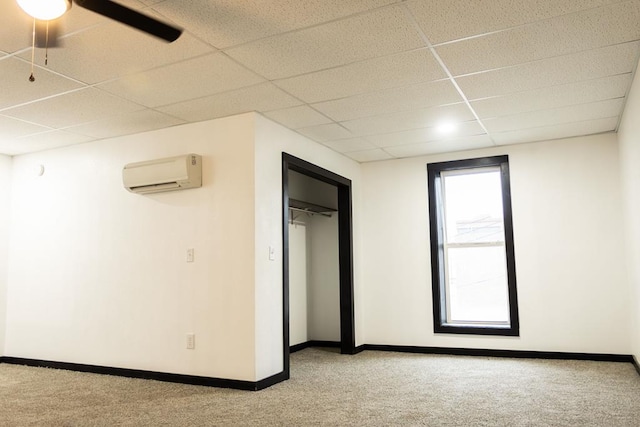 unfurnished bedroom featuring light carpet, a paneled ceiling, a wall unit AC, ceiling fan, and a closet