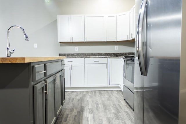 kitchen featuring dark stone countertops, white cabinetry, light hardwood / wood-style flooring, and appliances with stainless steel finishes