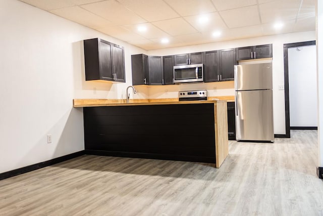 kitchen with sink, a drop ceiling, stainless steel appliances, light hardwood / wood-style flooring, and kitchen peninsula