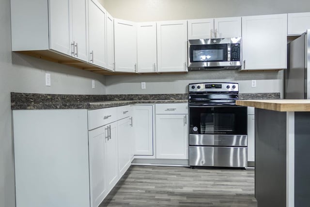 kitchen featuring white cabinets, appliances with stainless steel finishes, light hardwood / wood-style floors, and dark stone counters