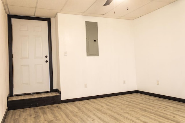 empty room with light wood-type flooring, electric panel, a drop ceiling, and ceiling fan