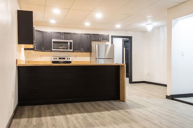 kitchen with kitchen peninsula, appliances with stainless steel finishes, a paneled ceiling, and light hardwood / wood-style floors