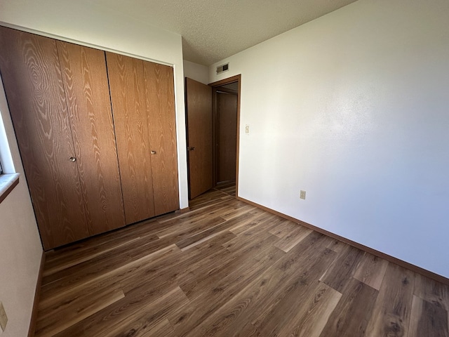 unfurnished bedroom featuring dark wood-type flooring, a textured ceiling, and a closet