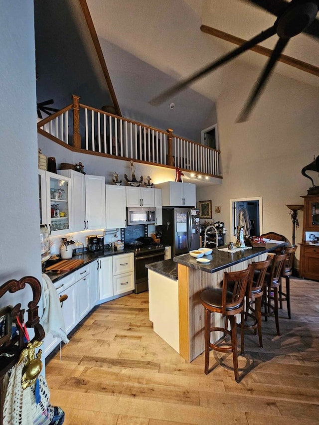 kitchen featuring appliances with stainless steel finishes, a breakfast bar, light hardwood / wood-style floors, white cabinetry, and an island with sink