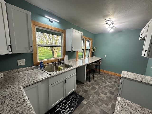kitchen with a textured ceiling, a sink, baseboards, white cabinetry, and light stone countertops