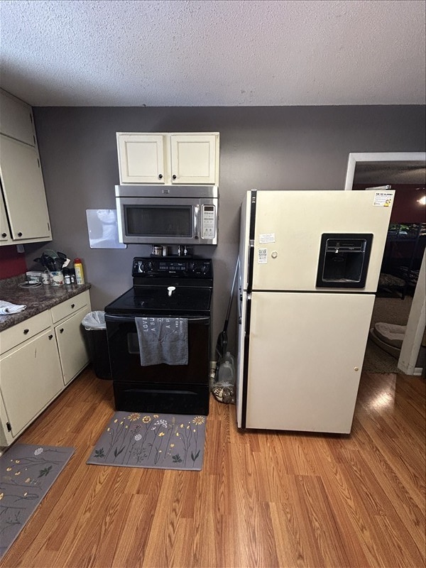116 Adams St, Centralia, MO 65240 - kitchen featuring stainless steel microwave, black range with electric cooktop, freestanding refrigerator, light wood-type flooring, and white cabinetry