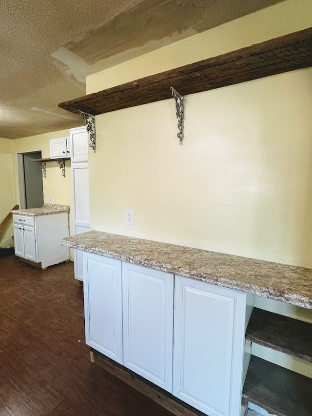 kitchen with light stone counters, a textured ceiling, white cabinets, and dark hardwood / wood-style floors