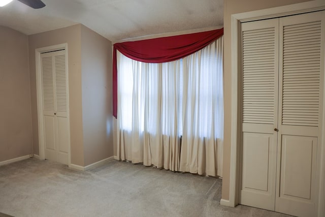 unfurnished bedroom featuring ceiling fan, light colored carpet, and multiple closets