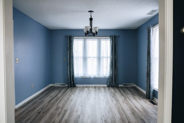 unfurnished room with light hardwood / wood-style floors, a textured ceiling, and an inviting chandelier