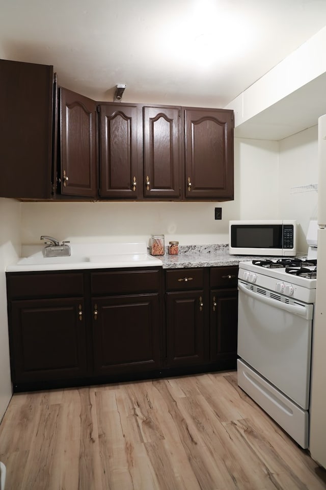 kitchen featuring dark brown cabinetry, white appliances, and light hardwood / wood-style flooring