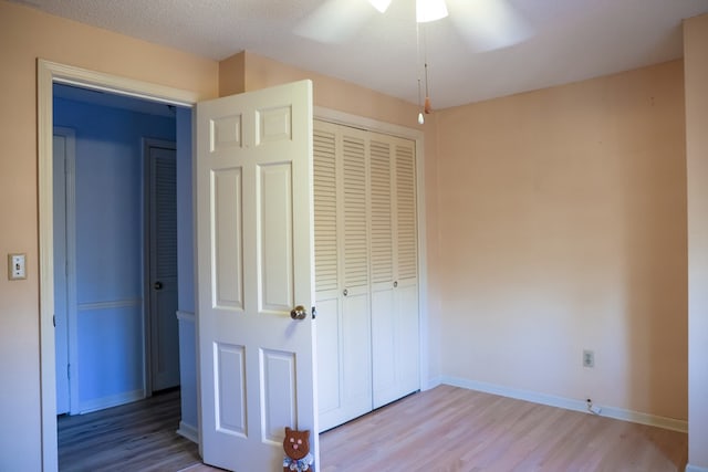 unfurnished bedroom with ceiling fan, a closet, light hardwood / wood-style floors, and a textured ceiling