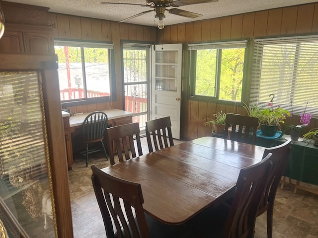 dining room with ceiling fan, a textured ceiling, and wooden walls