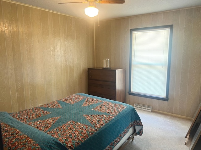 carpeted bedroom with ceiling fan and wood walls